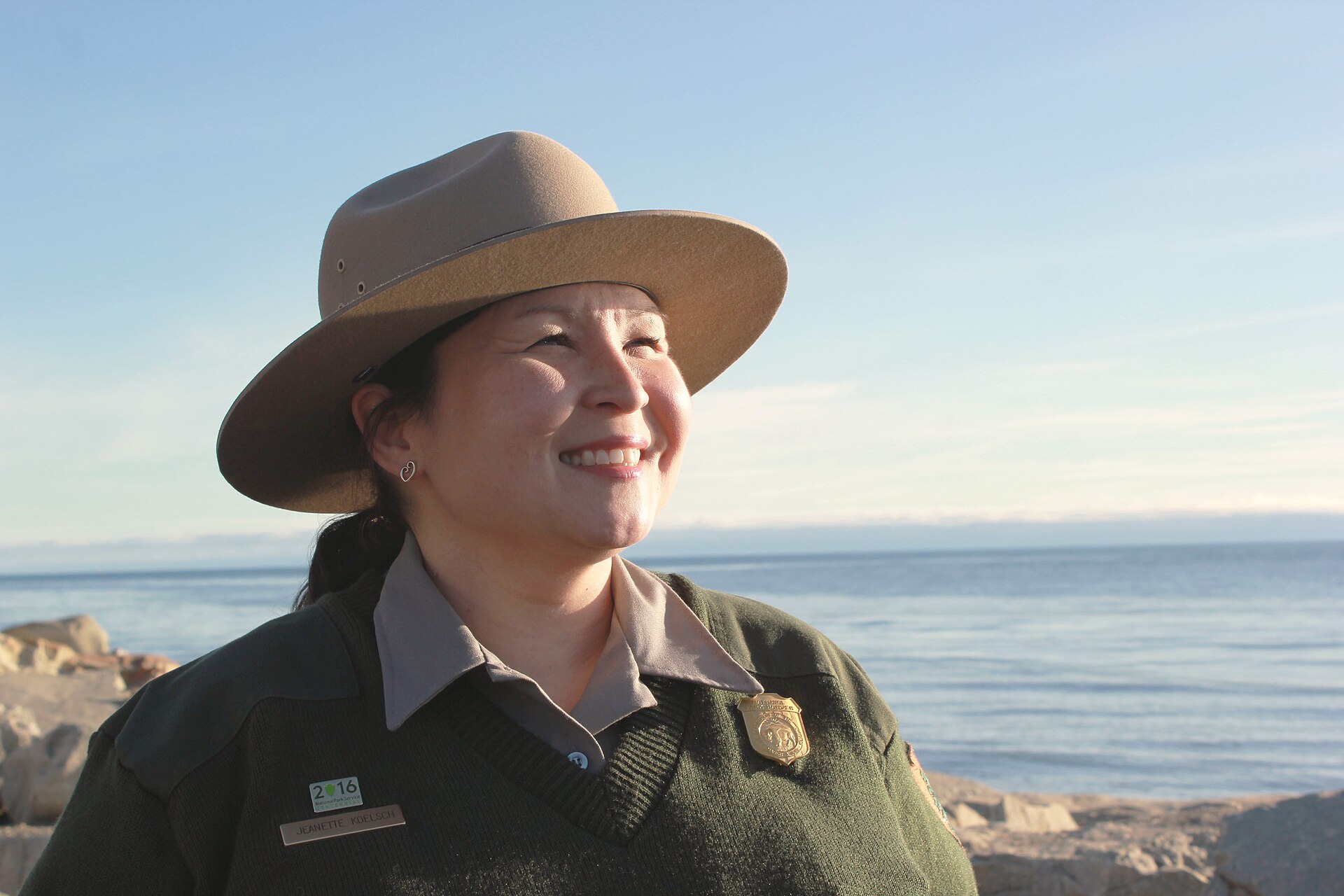 Portrait of Jeanette Koelsch beside the Bering Sea on a sunny day. Portrait of Jeanette Koelsch beside the Bering Sea. Jeanette Koelsch was born in Anchorage, Alaska to Joe and Grace Cross, and moved to Nome in 1982 when she was about ten years old. Her maternal grandparents were Jane and Jack Antoghame from St. Lawrence Island. After graduating from Nome-Beltz Senior High School, she attended Linfield College in McMinnville, Oregon, graduating with an undergraduate degree in general science. Her first professional job after college was in 1994 as a summer seasonal park ranger with the National Park Service at Bering Land Bridge National Preserve. Her duties included escorting scientific research projects into the field. Within a year, Jeanette was also working as an interpretive ranger during the winter months where she helped develop educational curriculum and hosted school programs in Nome and the surrounding villages. By 1996, she was hired full time as the interpretive park ranger, and eventually won the Alaska Region Freeman Tilden Award for her educational work, including a PBS documentary and a CD-ROM program called "Science in Our Lives" that included oral history interviews with elders, combining scientific and cultural elements, and games for children. From 1998 to 2009, Jeanette worked for Kawerak Incorporated helping to develop economic development plans for their villages. Since 2009, she has served as the superintendent of Bering Land Bridge National Preserve where she is proud to play a role in promoting good stewardship of park resources both to local community members and the visiting public. Keywords: Bering Land Bridge National Preserve